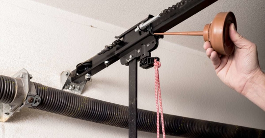 Man oils the quick release of a garage door opener to keep it working smoothly