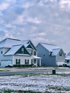 Snowy houses stand in a suburban neighborhood under a cloudy sky.